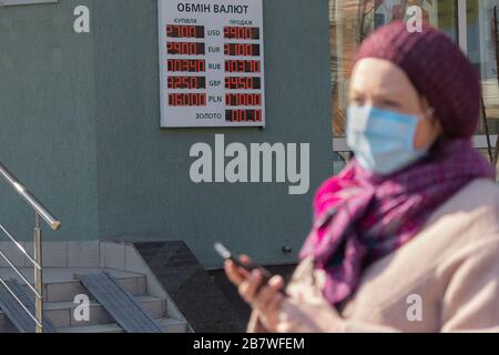 Kiev, Ucraina - 18 marzo 2020: Donna in maschera medica cammina oltre il tabellone con un tasso di cambio valuta durante la quarantena Foto Stock