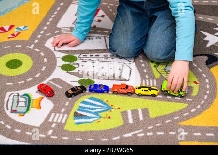 Ragazzo di cinque anni che gioca e allineano le auto giocattolo su un tappetino da gioco con le strade. Il ragazzo è vestito di jeans blu e tiene un giocattolo ambulanza. Foto Stock