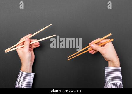 Immagine creativa delle bacchette di legno in due mani maschio su sfondo nero. Il giapponese e il cinese del cibo con copia spazio. Foto Stock