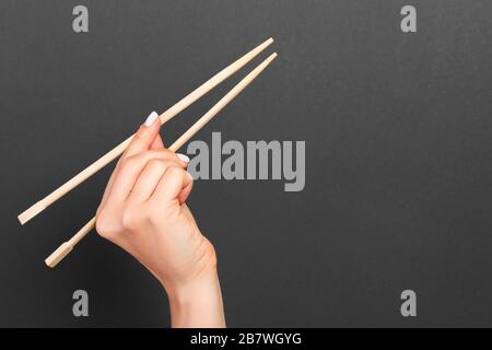 Immagine creativa delle bacchette di legno nelle femmine di mano su sfondo nero. Il giapponese e il cinese del cibo con copia spazio. Foto Stock