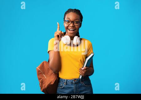 Studente ragazza che punta dito in su avendo momento Eureka, sfondo blu Foto Stock