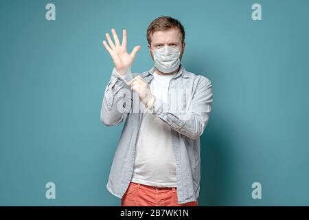 Uomo serio in una maschera medica, mette su guanti di lattice, per proteggere contro un virus pericoloso. Concetto di salute e sicurezza. Foto Stock