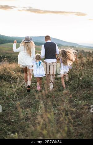 Indietro foto di famiglia allegra in abiti alla moda, genitori e bambini, godendosi e correndo insieme in montagna. Famiglia in Foto Stock