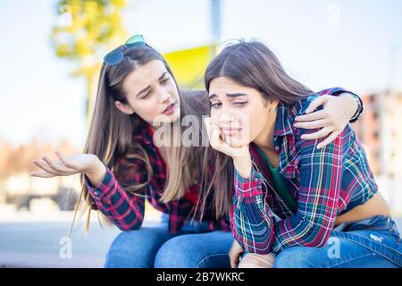 Giovane donna conforta una triste amica femminile nel parco Foto Stock