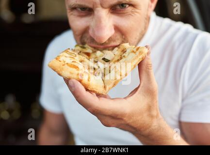 Vista ravvicinata dell'uomo affamato che mangia un pezzo di pizza Foto Stock