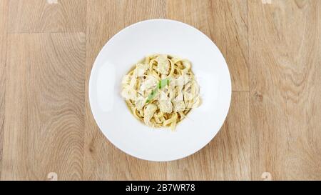 pasta alfredo con foglie di basilico e parmigiano in un piatto bianco su fondo ligneo Foto Stock