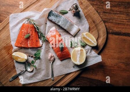 Salmone crudo fresco con limone, erbe e spezie su carta sul tagliere. Preparazione del cibo. Foto Stock