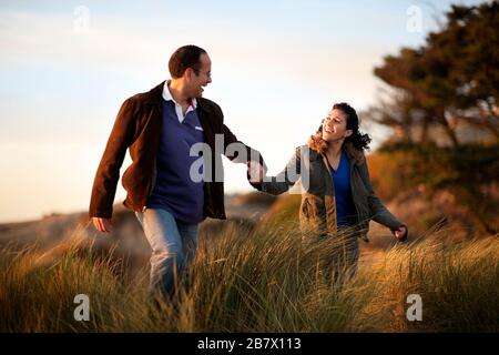 Felice metà adulto giovane tenendo le mani mentre si cammina attraverso erba lunga. Foto Stock