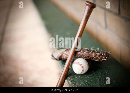 Mitretto da baseball in pelle, mazze da baseball e palla su una panca di legno verde. Foto Stock