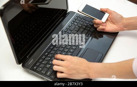 Mani che usano il portatile e il telefono per fare acquisti online, immagine pulita di fronte alla finestra in luce soffusa Foto Stock