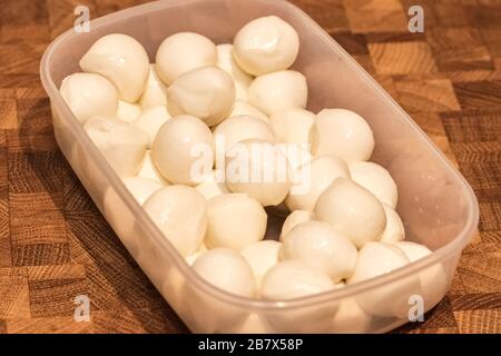 Mini sfere di mozzarella in un piatto di plastica su un tavolo di legno. Ingrediente per insalata Foto Stock
