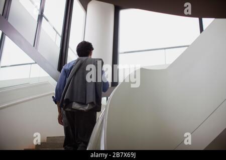 Uomo d'affari stanco che cammina su una rampa di scale all'interno di un edificio. Foto Stock