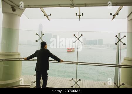 Uomo d'affari di mezza età su una piattaforma panoramica che si affaccia su un porto cittadino. Foto Stock