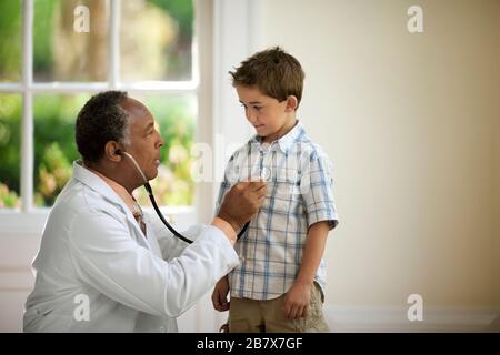 Medico senior che ascolta il battito cardiaco di un giovane paziente con uno stetoscopio. Foto Stock