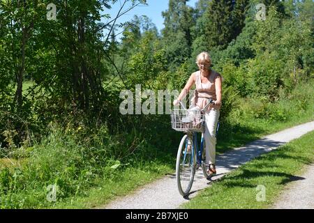Una donna anziana che guida una bicicletta su una strada sterrata, Boda kyrkby, Rattvik, Dalarna Foto Stock
