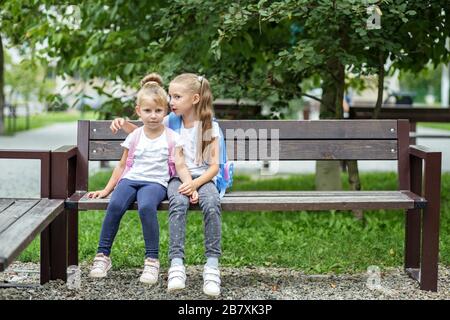 Due bambini piccoli raccontano i segreti su una panchina. Il concetto è di ritorno a scuola, famiglia, amicizia e infanzia. Foto Stock