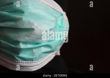 Un misterioso individuo con cappuccio irriconoscibile con felpa scura indossa una normale maschera chirurgica blu in italia Foto Stock