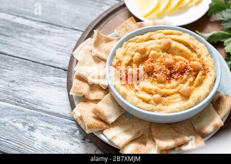 Una ciotola di cremoso hummus fatto in casa con olio d'oliva e patatine di pita. Tradizionale pasto vegano sano. Foto Stock