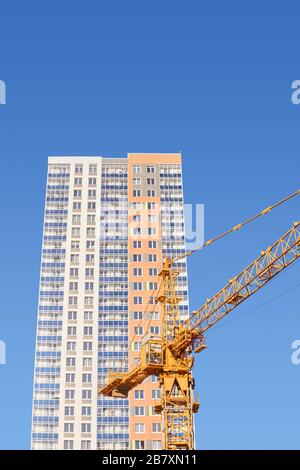 costruzione a più piani - cabina e braccio di una gru a torre e la parte superiore di un edificio residenziale multi-appartamento di nuova costruzione contro il blu Foto Stock
