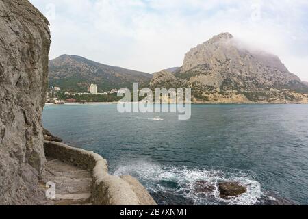 Sentiero di Golitsyn lastricato in pietra nel villaggio turistico di Novy Svet e scogliere costiere nella Crimea. Giorno nuvoloso all'inizio della primavera Foto Stock