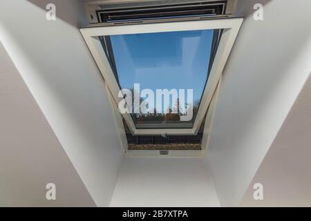 Vista ravvicinata della finestra a tetto aperto isolata con vista degli alberi sullo sfondo blu del cielo. Foto Stock