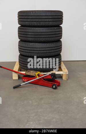 Primo piano pneumatici auto su ruote di stoccaggio su un pallet e un martinetto di sostituzione pneumatici. Scatola di riparazione auto. Gli sfondi di trasporto. Foto Stock