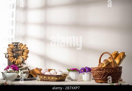 Ancora la vita con il cibo russo panini bagels marshmallows e samovar con stand tè sul tavolo su sfondo di parete bianca in cucina con luce del sole. Conc Foto Stock