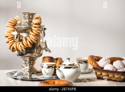 Ancora la vita con il cibo russo panini bagels marshmallows e samovar con stand tè sul tavolo su sfondo di parete bianca in cucina con luce del sole. Conc Foto Stock