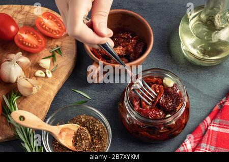 La mano femminile mette i pomodori a forcella in un vaso di vetro con una forchetta. Cottura in scatola di pomodori a scatti con spezie Foto Stock