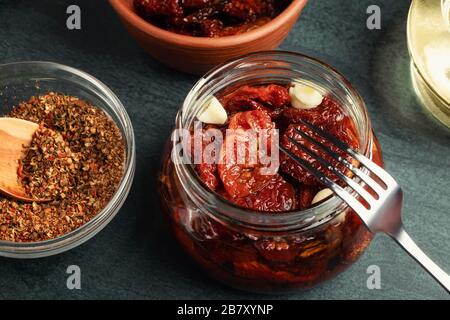 Cucinare i pomodori secchi in un vaso di vetro con olio d'oliva, aglio e spezie. Foto Stock