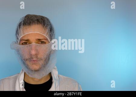 Un maschio adulto vestito in un camice bianco da laboratorio con una rete di capelli e una rete di barba sopra. Pronto per lavorare in una camera bianca o in un laboratorio Foto Stock