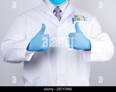 il medico in un cappotto bianco e cravatta mostra con la sua mano un gesto come, indossando i guanti medici blu del lattice, primo piano Foto Stock