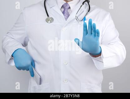 medico maschile in un cappotto bianco e guanti blu sterile mostra un gesto stop con la sua mano, sfondo bianco Foto Stock