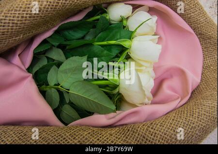 Bouquet di rose bianche sulla carta da imballaggio in tessuto naturale. Fiori di primavera sullo sfondo del sughero . Vista dall'alto con posto per il testo. Spazio di copia. Foto Stock