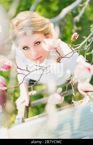 giovane donna che guarda attraverso i rami di un albero con fiori rosa Foto Stock
