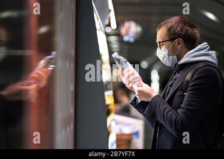 Uomo caucasico cliente in occhiali che indossano maschera di protezione facciale, l'acquisto e la scelta della bottiglia d'acqua, legge le informazioni su un'etichetta. Acquisto di cibo dur Foto Stock