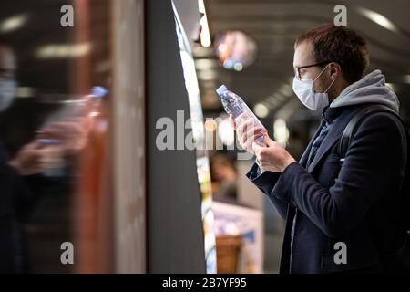 Uomo caucasico cliente in occhiali che indossano maschera di protezione facciale, l'acquisto e la scelta della bottiglia d'acqua, legge le informazioni su un'etichetta. Acquisto di cibo dur Foto Stock