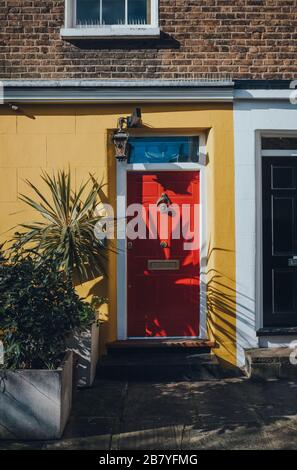 Colorato e luminoso porta d'ingresso rosso su una casa gialla a Londra, Regno Unito. Foto Stock