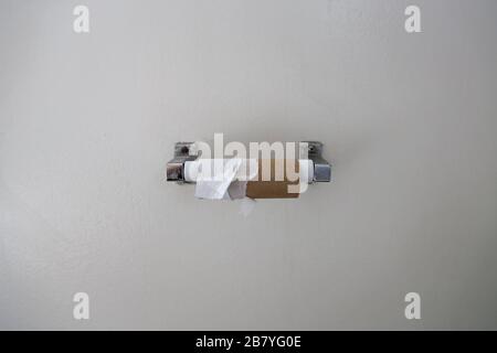 I residui strappati di un rotolo di carta igienica sono mostrati su un dispenser montato sulla parete bianca di un bagno. Foto Stock