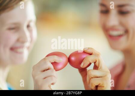 Primo piano su madre felice e la figlia che hanno spillare le uova con uova di pasqua rosse in casa nella soleggiata giornata primaverile. Foto Stock
