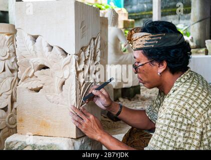 Un artigiano Balinese in un duro lavoro a scolpire una statua di un blocco di pietra Foto Stock