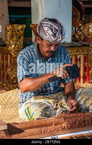 Un artigiano Balinese in un duro lavoro a scolpire una statua di un blocco di legno utilizzando un martello e scalpello. Foto Stock