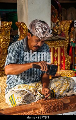 Un artigiano Balinese in un duro lavoro a scolpire una statua di un blocco di legno utilizzando un martello e scalpello. Foto Stock