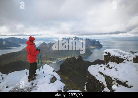 Giovane donna in giacca rossa con bastoni da trekking sulla neve montagna Foto Stock