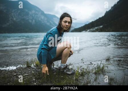 Giovane donna accovacciata sul lago di garda Foto Stock