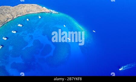 Il Cratere Molokini, colpo aereo dell'isolotto a forma di mezzaluna che mostra il dito sommerso conosciuto come barriere coralline finiscono a metà mattina con barche charter, Maui, Haw Foto Stock