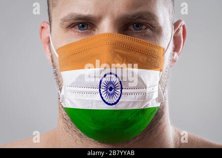 Giovane uomo con occhi dolorosi in una maschera medica dipinta nei colori della bandiera nazionale dell'India. Protezione medica contro le malattie dell'aria, coronavi Foto Stock