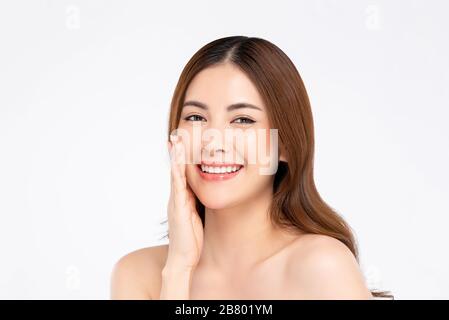 Beauty shot di sorridente modello donna asiatica con pelle chiara e discreta facendo mano toccare la posa del viso in bianco isolato sfondo per il concetto di cura della pelle Foto Stock