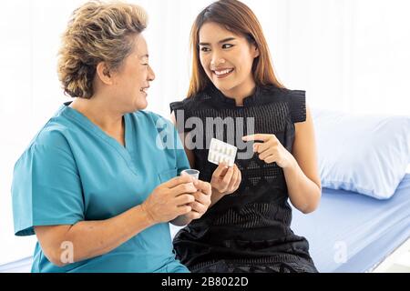 Chiusura del caregiver donna aiutando vecchia donna anziana prendendo pillola di medicina sul letto e controllare fino a casa. Foto Stock