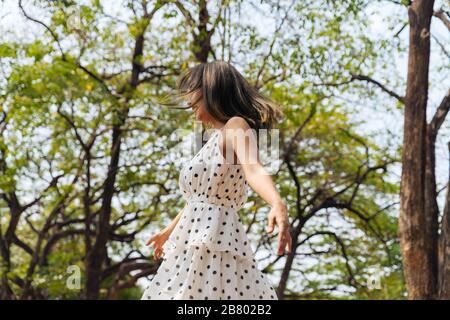 Felice e spensierata giovane donna anni '20 ballare nella foresta all'aperto con alberi verdi. Ritratto di bella ragazza rilassante. Concetto di libertà e felicità Foto Stock